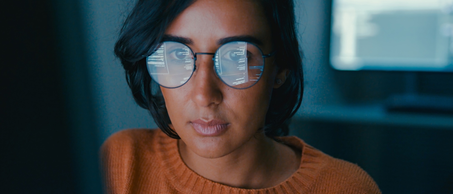 A woman looking at a computer with the screen reflected in her glasses