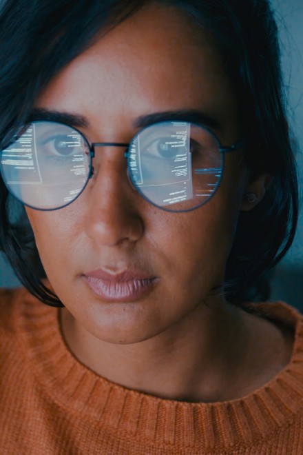 A woman looking at a computer with the screen reflected in her glasses