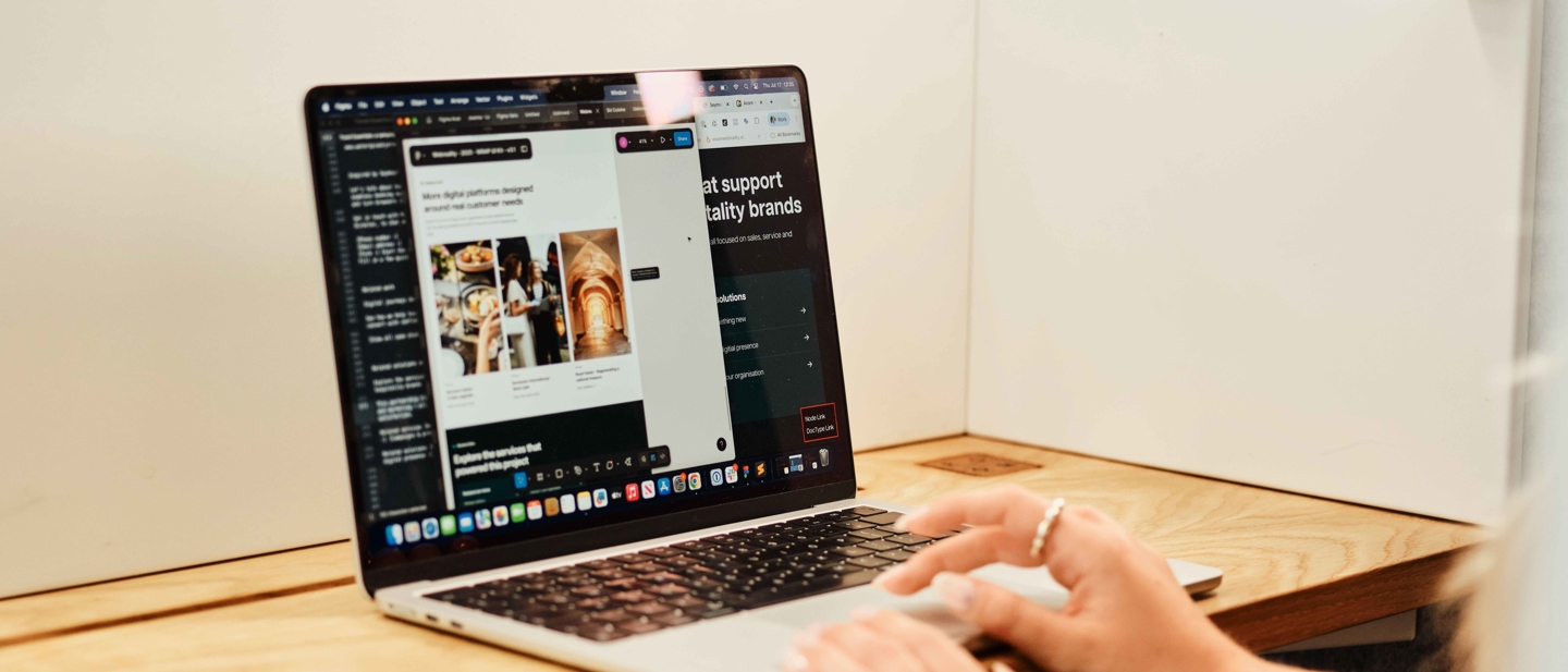 Close-up of a laptop showing a website design preview and editor side by side on a wooden desk.